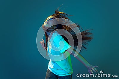 Young astonished girl with long loose hair dancing isolated on blue background in neon light. Concept of beauty, art Stock Photo
