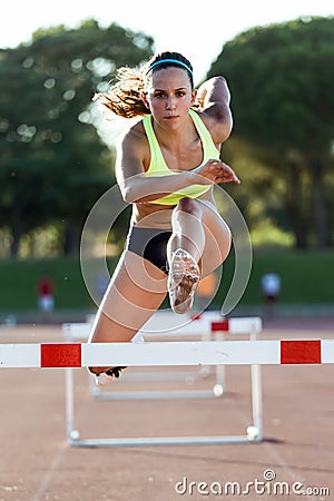 Young athlete jumping over a hurdle during training on race trac Stock Photo