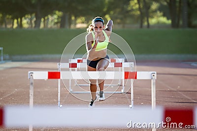 Young athlete jumping over a hurdle during training on race trac Stock Photo