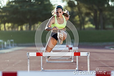 Young athlete jumping over a hurdle during training on race trac Stock Photo