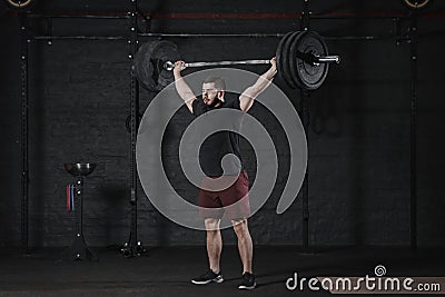 Young athlete lifting barbell overhead at the crossfit gym. Handsome man doing functional training.Practicing powerlifting. Worko Stock Photo