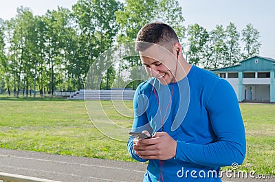 A young athlete writes a message on the smartphone after training and listens to music Stock Photo