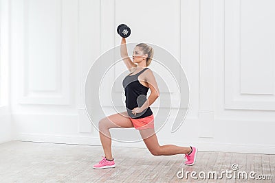 Young athletic beautiful blonde woman wearing pink shorts and black top holding dumbbell. Stock Photo