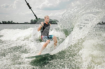 Young athletic man wakesurfing on the board holding a cable Stock Photo