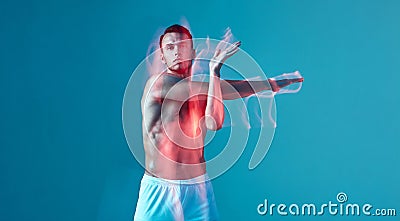 A young athletic, pumped-up man does a warm-up. A man with a bare torso and white shorts on a blue background. Stock Photo