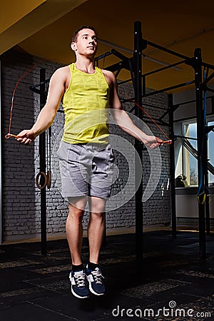 Young athletic sportsman in the sportwear working with jumping rope in cross fit gym against brick wall. Stock Photo