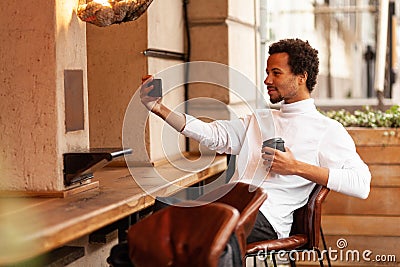 Young attractive african man takes selfie picture in city street cafe Stock Photo