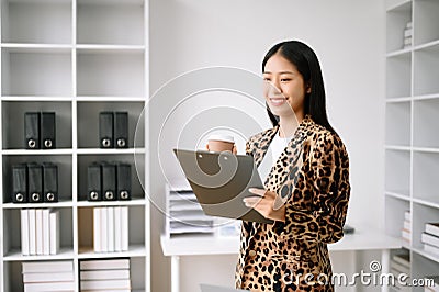 Young attractive Asian female office worker business suits smiling at camera with working notepad, tablet and laptop documents . Stock Photo