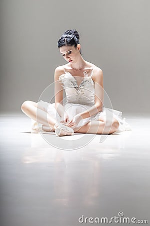Young attractive ballerina sitting on the floor working with her pointed ballet shoes Stock Photo