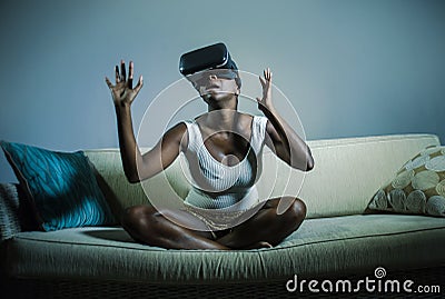 Young attractive black afro American woman playing amazed and surprised virtual reality video game wearing VR goggles Stock Photo