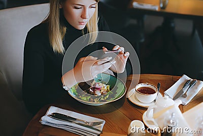 Young attractive blonde woman uses phone at dinner in restaurant Stock Photo