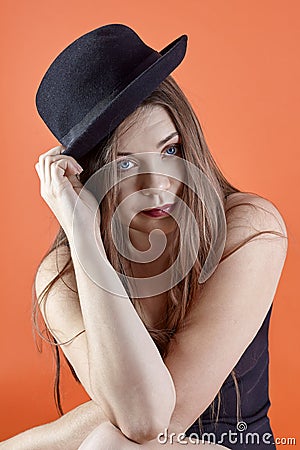 Young attractive caucasian brunette woman with bright blue eyes and dark lipstick, touches the black bowler hat, looking right to Stock Photo