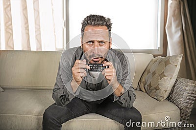 Young attractive concentrated and focused man watching television news or thriller movie sitting at living room sofa couch Stock Photo