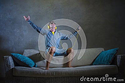 Young attractive and cool happy man listening to techno music with yellow headphones jumped on top of home sofa couch dancing inte Stock Photo