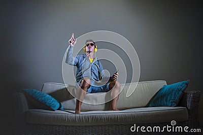 Young attractive and cool happy man listening to techno music with yellow headphones jumped on top of home sofa couch dancing inte Stock Photo