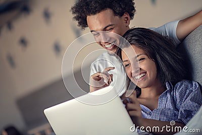 Young attractive diverse couple browsing internet, using laptop computer, smiling. Stock Photo