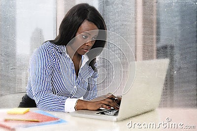 Young attractive and efficient black ethnicity woman sitting at business district office computer laptop desk typing Stock Photo