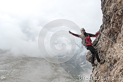 Young female climber on a vertical and exposed rock face smiling and making a peace sign Stock Photo