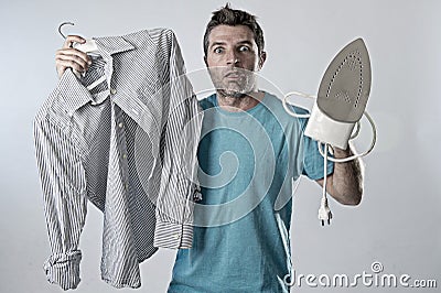 Young attractive and frustrated man holding iron and shirt stressed and tired in bored and lazy face Stock Photo