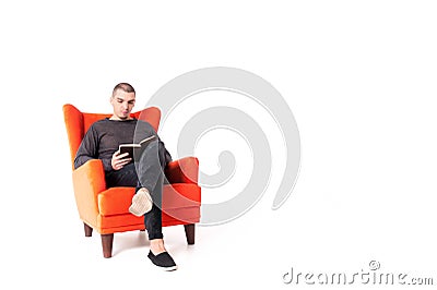 A young attractive guy is sitting on a red armchair and reading a book. Isolated on a white background. Copy space Stock Photo