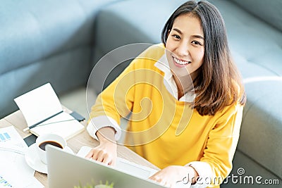 Young attractive happy asian female student sitting at living room floor smiling and looking up at camera Stock Photo