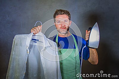 Young attractive happy and proud house husband or single man holding iron showing shirt after ironing on studio backgroun Stock Photo