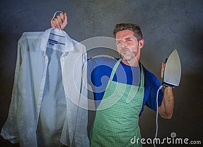 Young attractive happy and proud house husband or single man holding iron showing shirt after ironing on studio backgroun Stock Photo