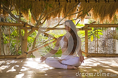 Young attractive and happy relaxed woman doing yoga and meditation exercise sitting in lotus position outdoors at wooden hut Stock Photo