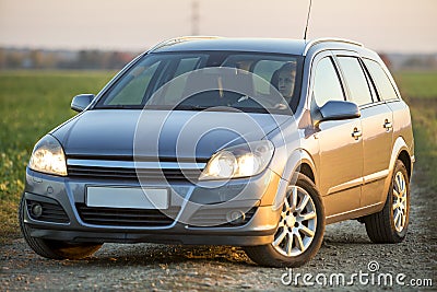 Young attractive long-haired woman inside shiny silver car at steering wheel on gravel empty road on bright blurred summer sunny Stock Photo