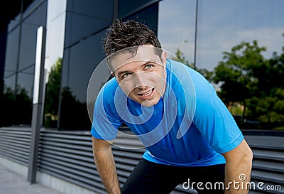 Young attractive man leaning exhausted after running session sweating taking a break to recover in urban street Stock Photo