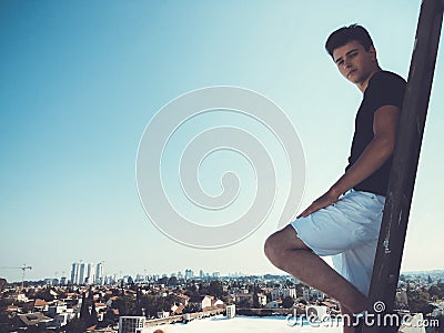 Young attractive man posing in front of camera on the roof of a residential building standing on a ladder Stock Photo