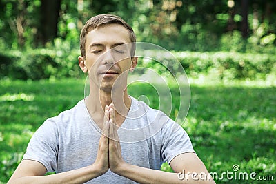 Attractive man in sport clothes is meditating cupped in a meditation or prayer gesture with a pacified face in the park Stock Photo