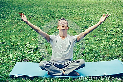 Young attractive man in sport clothes is meditating in the lotus position with a pacified face in the park against the background Stock Photo