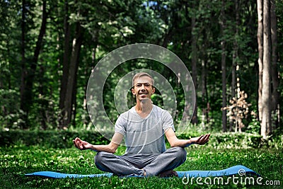 Young attractive man in sport clothes is meditating in the lotus position with a pacified face in the park Stock Photo