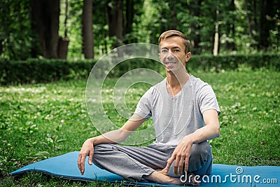 Young attractive man in sport clothes is meditating in the lotus position with a pacified face in the park Stock Photo
