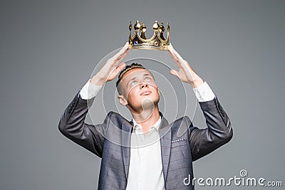Young attractive man in a suit holding above his head a golden crown on a gray background Stock Photo