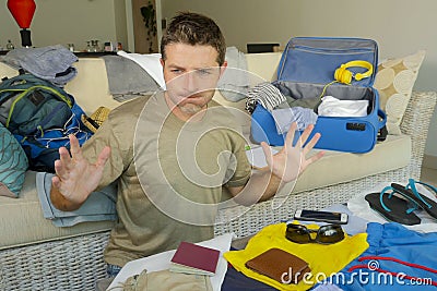 Young attractive and messy man at home couch preparing travel back and suitcase with passport , clothes and things mess looking st Stock Photo