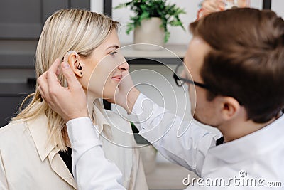 A young attractive otolaryngologist doctor gives a consultation to a female patient. A doctor explains how to wear a hearing aid Stock Photo