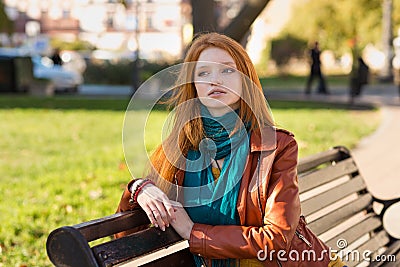 Young attractive pensive woman sitting on bench in the park Stock Photo