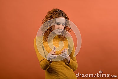 Young and attractive redhead Caucasian girl in orange jumper showing hands with fingers pistols isolated on orange studio backgrou Stock Photo