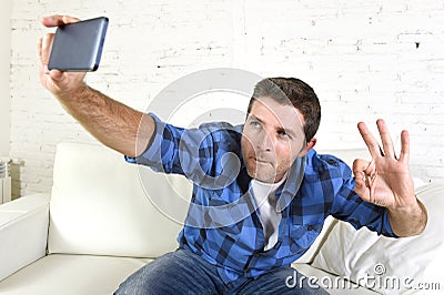 Young attractive 30s man taking selfie picture or self video with mobile phone at home sitting on couch smiling happy Stock Photo