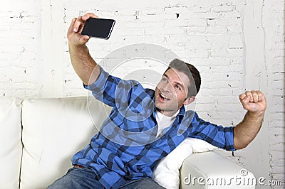 Young attractive 30s man taking selfie picture or self video with mobile phone at home sitting on couch smiling happy Stock Photo