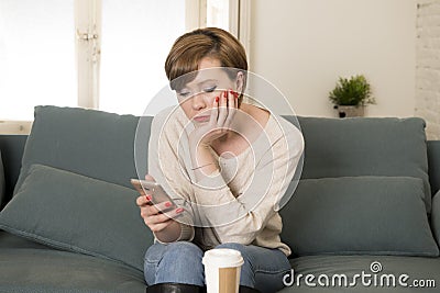 Young attractive 30s red hair woman upset bored and moody using internet app on mobile phone sitting at home sofa couch in annoyed Stock Photo