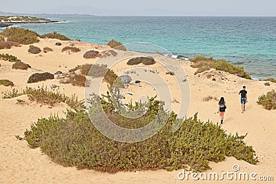Young heterosexual couple walking towards shore on sandy beach with shrubs Editorial Stock Photo