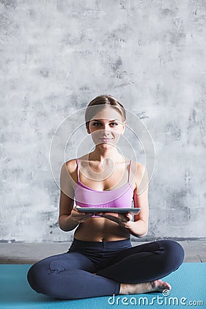 Young attractive sporty woman sitting on mat, holding digital tablet in her hands Stock Photo