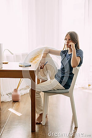 A young attractive student talks on a smartphone while studying at home, discusses homework or a joint project with Stock Photo