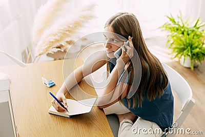 A young attractive student talks on a smartphone while studying at home, discusses homework or a joint project with Stock Photo