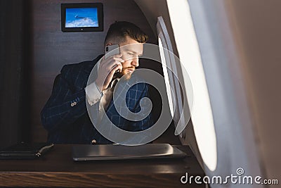 Young attractive and successful businessman talking on the phone and working while sitting in the chair of his private Stock Photo