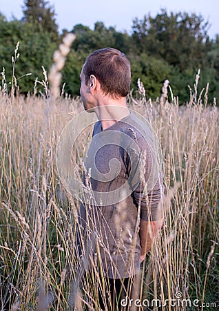 A young attractive thin guy standing in the tall grass on the forest background. Stock Photo