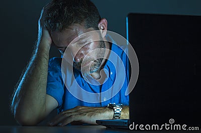 Young attractive and tired unshaven man working late night on laptop computer in the dark feeling frustrated and exhausted in Stock Photo